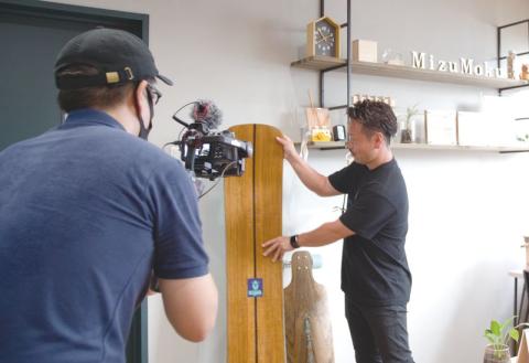 PR動画の撮影に臨む宮崎さん(右)。自社開発の木製スノーボードを手に様々な県産木材活用などの取り組みを紹介して
