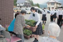 「てるさと」を訪れ、利用者代表のお年寄りにプランター植えの花を贈る中学生
